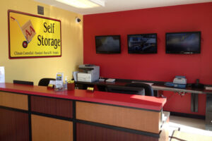 AA Self Storage office interior in Jacksonville NC showing front desk, red accent wall, and security monitor screens