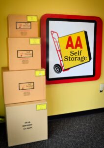 stacked moving boxes in various sizes with price tags next to AA Self Storage wall sign in the Jacksonville NC office